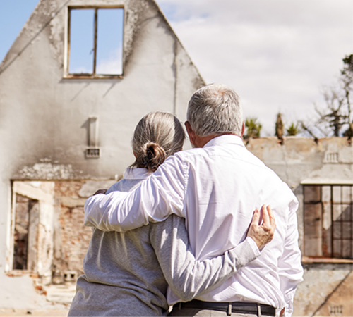 A woman and man hold each other as they look at their fire-damaged home.