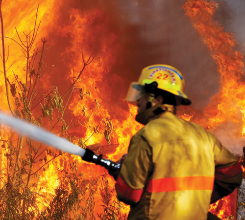 A firefighter with a water hose with a fire in the background